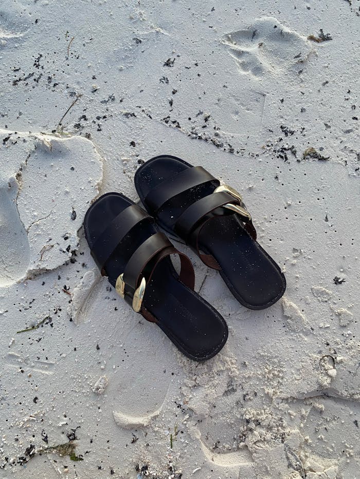 A pair of black sandals resting on a pristine white sand beach in the Maldives, capturing footprints and serenity.