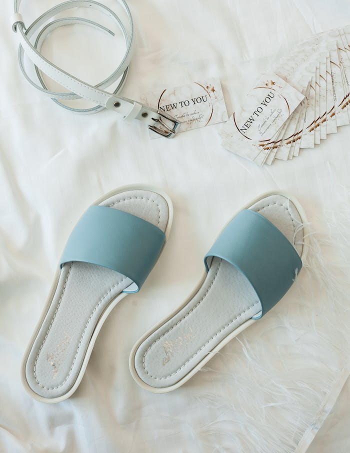A stylish flat lay featuring blue sandals and white leather belt on a white background.